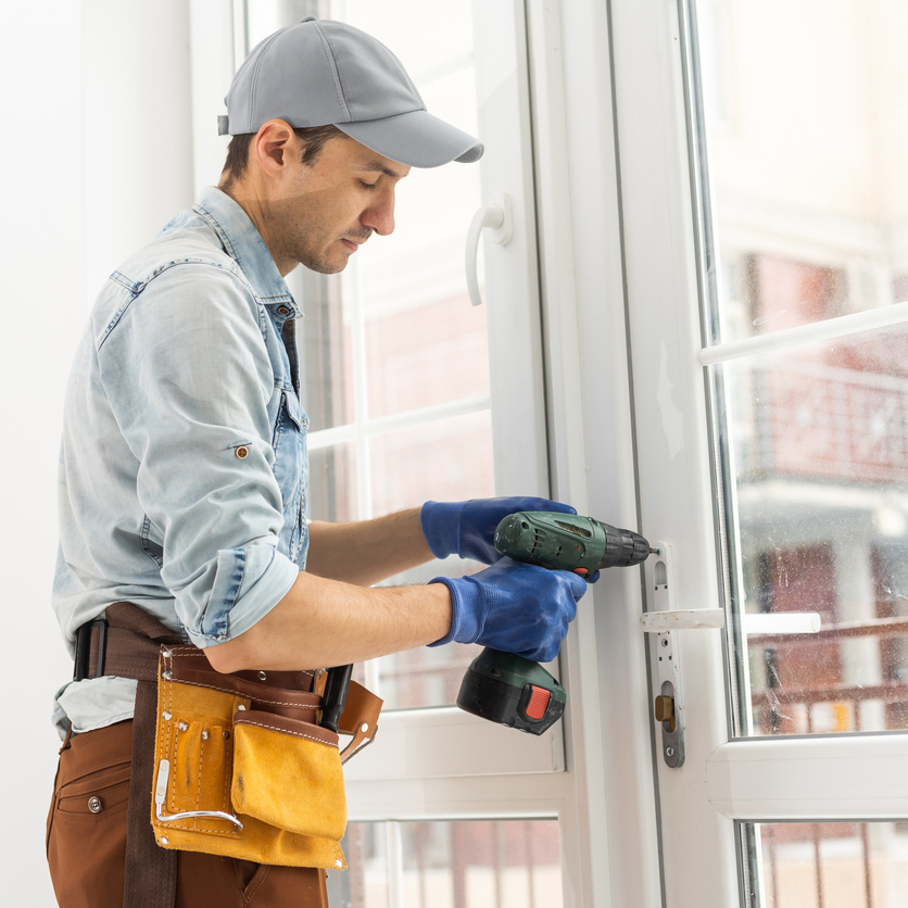 Man fixing lock to window with electric screwdriver.